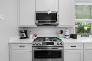 A kitchen with white cabinets, a stainless steel microwave, a gas stove, and a coffee maker. - Villa Mojito Lakefront Home + APTs Sleeps 24 (St. Augustine)
