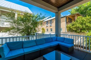 Un espace extérieur aménagé, abrité et doté d’un canapé bleu et d’une table en verre, offrant une vue sur un quartier résidentiel.