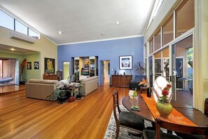 A spacious living room with a wooden floor, a dining area with a table and chairs, and a large window with a view. - Toogoom Beachfront (Toogoom)