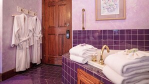A bathroom with a wooden door, purple tiles, a framed floral artwork, and towels. - Cliff Cottage Inn - Colette Queen Jacuzzi Suite (Eureka Springs)