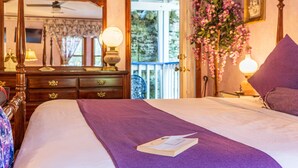 A bedroom with a four-poster bed, a dresser with drawers, a mirror, and a view of the outdoors. - Cliff Cottage Inn - Colette Queen Jacuzzi Suite (Eureka Springs)