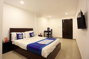 A bedroom with a bed, bedside table, chair, TV, and a door. - Hotel Global Star (New Delhi)