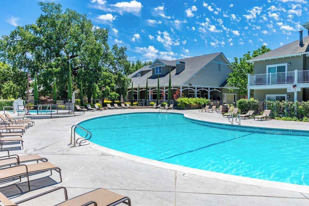 A swimming pool with lounge chairs, a covered area, and a building with a gabled roof.