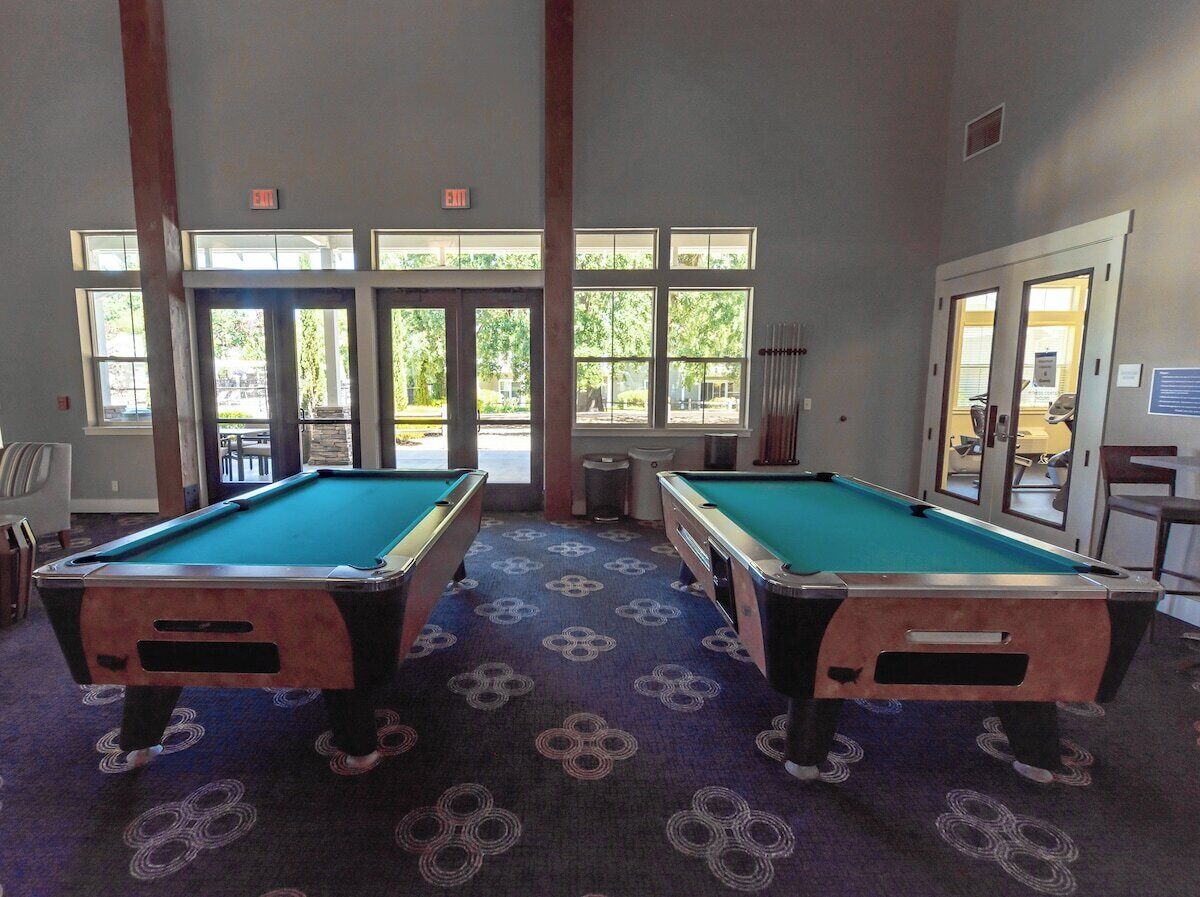 Une salle de billard équipée de deux tables de billard, dotée de grandes fenêtres et d’un sol recouvert de moquette.
