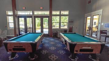 Une salle de billard équipée de deux tables de billard, dotée de grandes fenêtres et d’un sol recouvert de moquette.