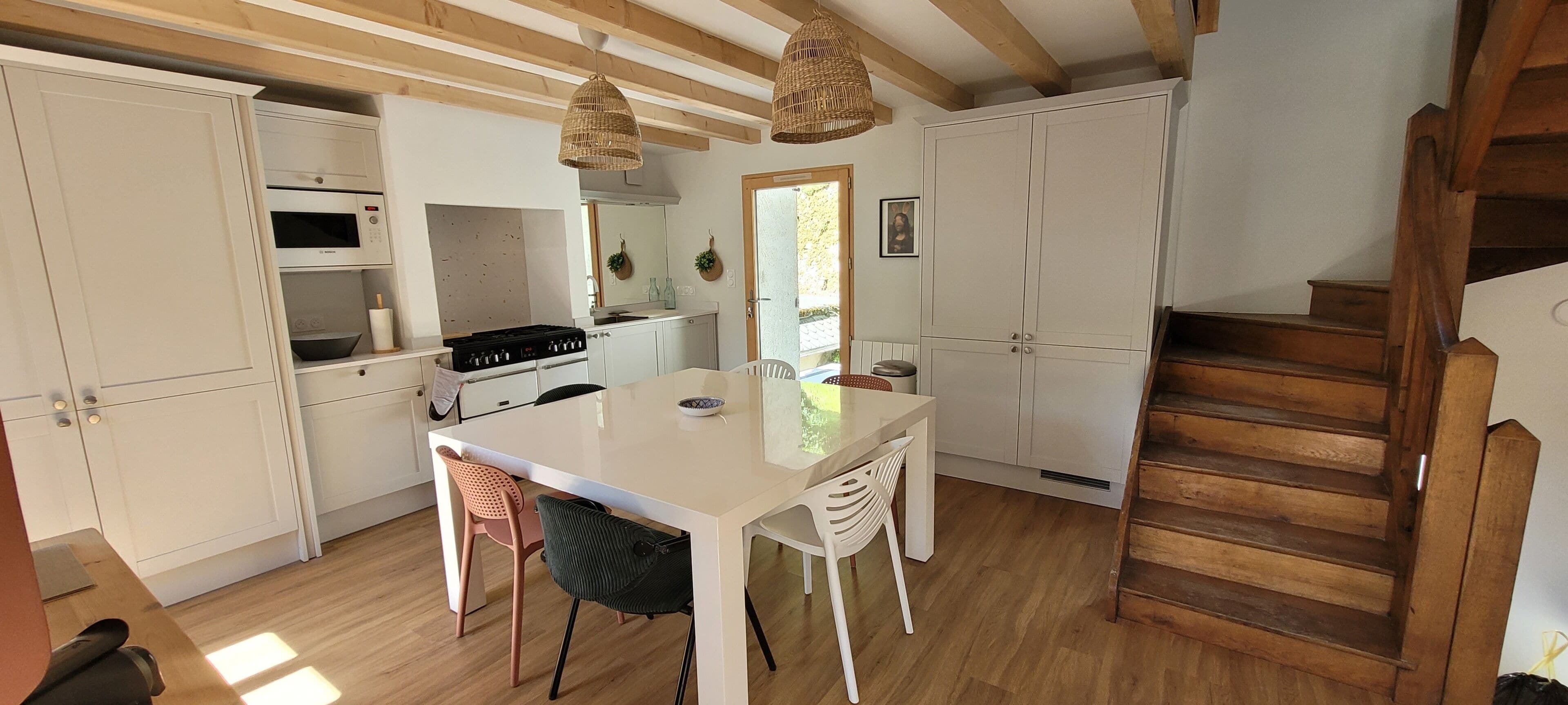 Una cocina con armarios blancos, una isla central, una estufa y lámparas de mimbre colgantes.