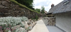 A stone wall with a pathway leading to a building with a grey roof. - House with a view of the mountains, St. Jacques des Blats, Lioran. (Saint-Jacques-des-Blats)