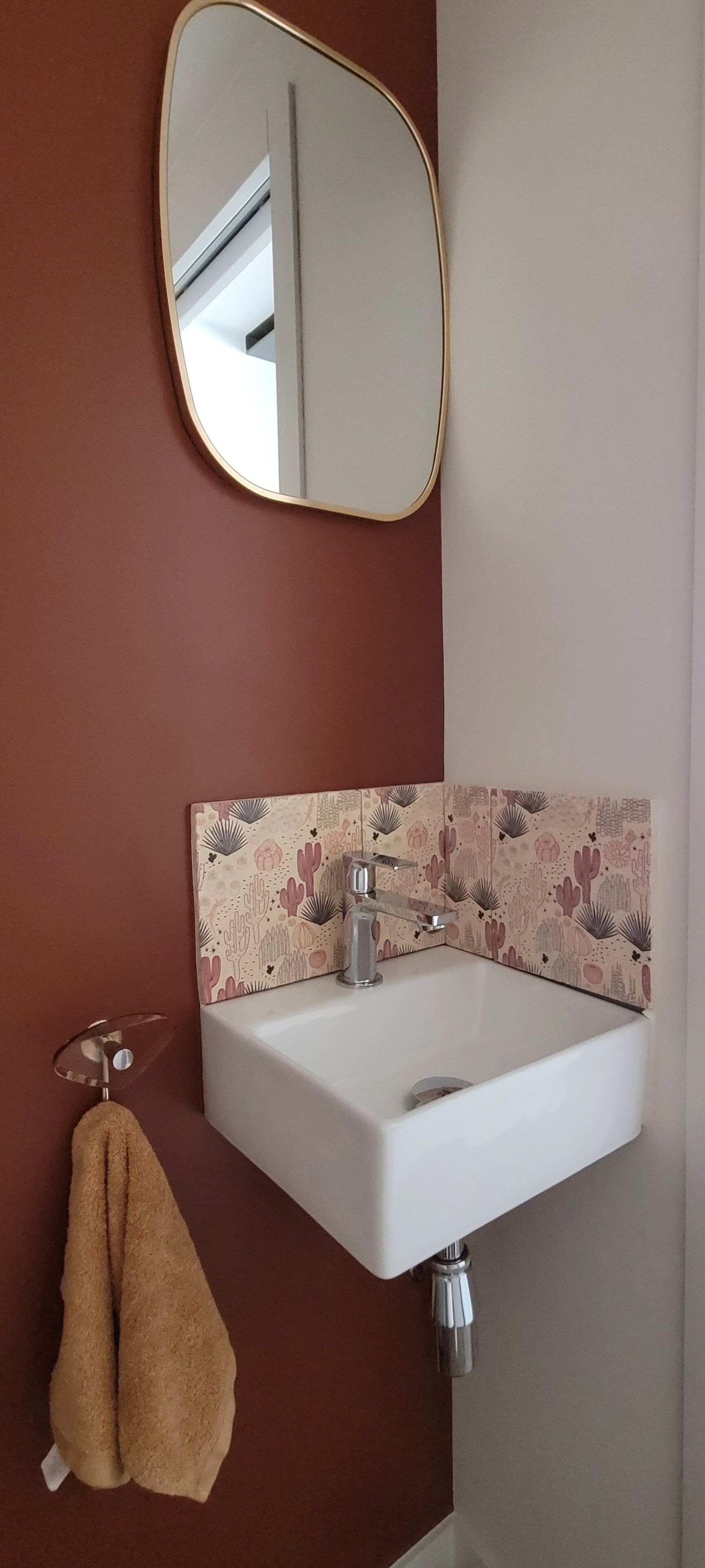 Une salle de bain avec un lavabo blanc, un miroir et un mur décoré d’un motif.