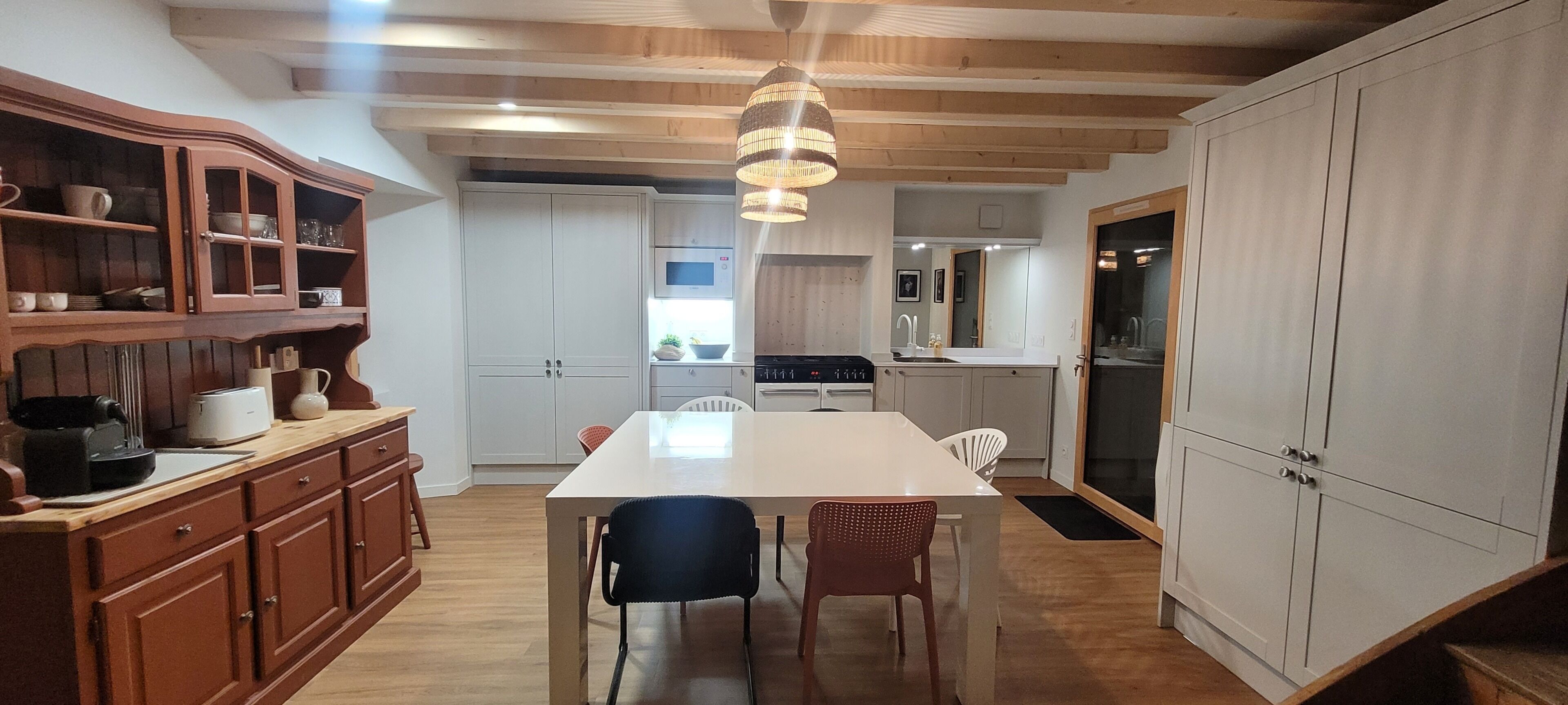 A kitchen with wooden cabinets, a dining table, chairs, and a hanging light fixture.