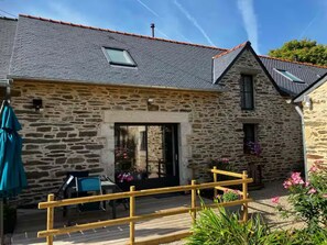 A stone building with a sloped roof, a wooden deck, and a small patio area with outdoor furniture. - T3, Sea view pool and jacuzzi, Le Pouldu (Clohars-Carnoët)