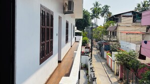 A residential building with a balcony, air conditioning units, and a paved pathway with potted plants.