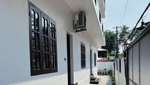 A narrow pathway leading to a building with a white exterior, black-framed windows, and a small set of steps.