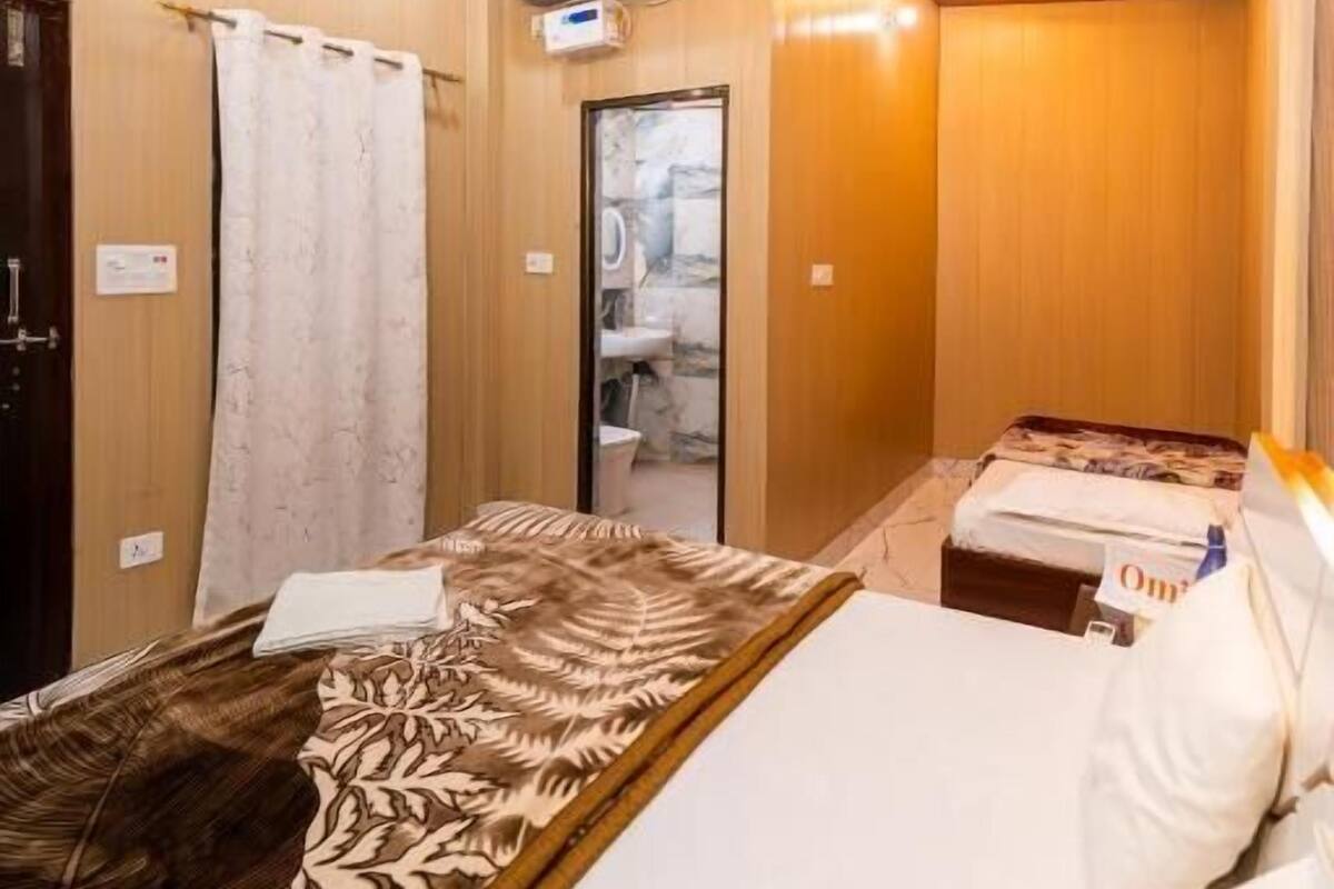 Habitación de hotel pequeña con cama, ventilador de techo, unidad de aire acondicionado y baño compacto.