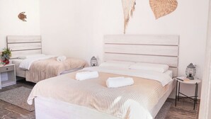 A bedroom with two beds, a bedside table with a lamp, a wall-mounted shelf, and a decorative wall hanging.