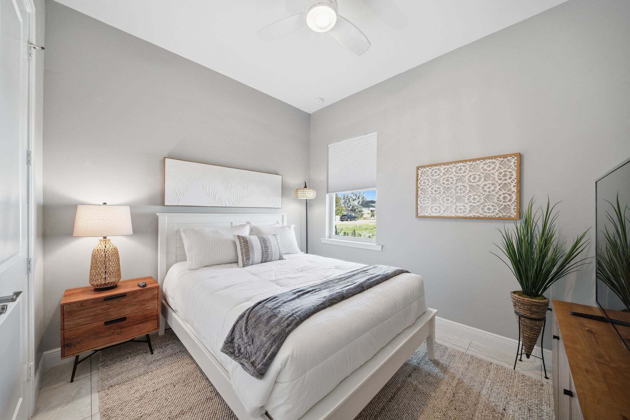 A bedroom with a bed, nightstand, lamp, and potted plant.