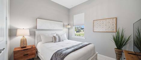 A bedroom with a bed, nightstand, lamp, and potted plant.