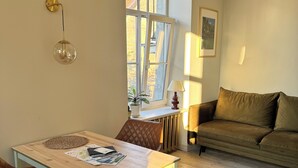Uma sala de estar com uma mesa de jantar, cadeiras de couro marrom, um sofá e uma janela com vista para edifícios.
