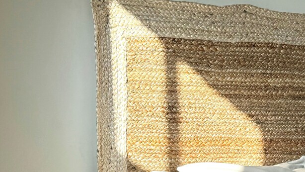 Uma cama com cabeceira trançada, roupa de cama branca e estrutura de madeira.