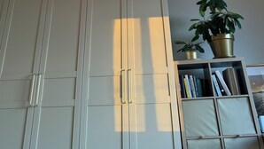 Quarto com um guarda-roupa branco grande, luminária pendente e estante com livros e uma planta em vaso.