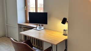 Um espaço de trabalho moderno com uma mesa de madeira, um monitor de computador, uma cadeira e uma janela com vista para edifícios.