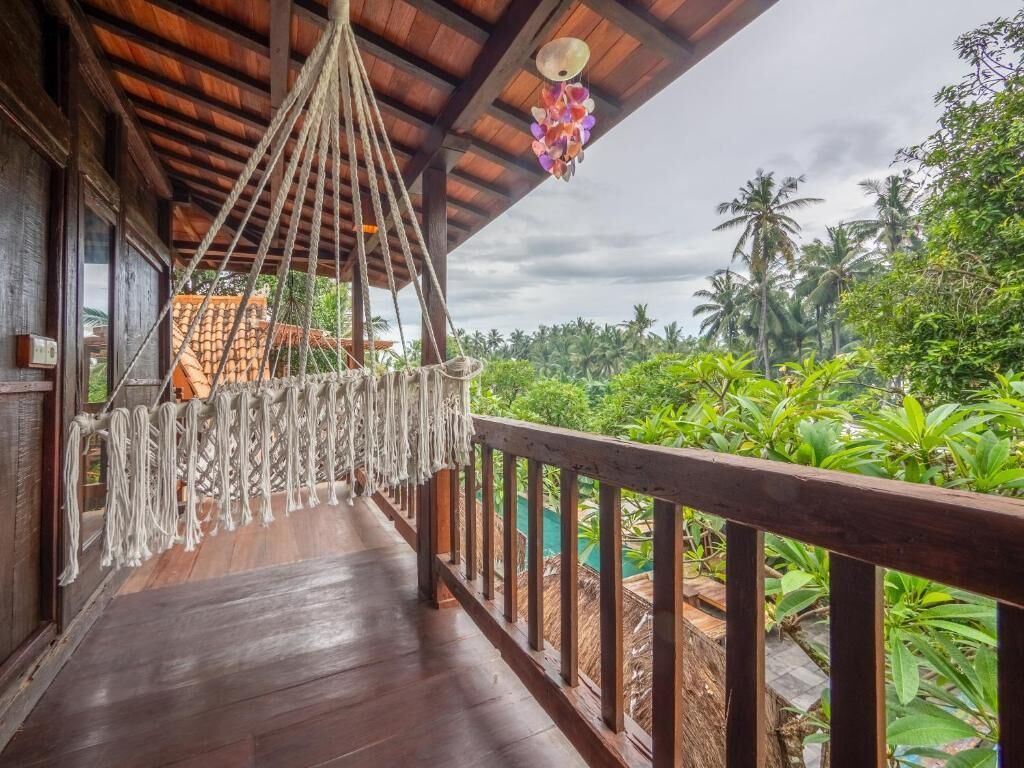A wooden deck with a hammock, wooden railings, and a view of lush greenery.