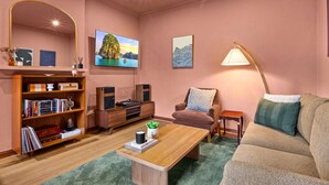 A cozy living room with a bookshelf, a coffee table, a sofa, a chair, a lamp, and artwork on the walls. - Stylish 1 Bed Apartment in East Melbourne (Melbourne)