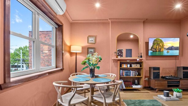 A room with a round table, chairs, a bookshelf, a TV, and a window with a view of buildings. - Stylish 1 Bed Apartment in East Melbourne (Melbourne)