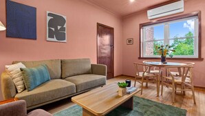A living room with a sofa, a coffee table, a dining table with chairs, a window with a view, and two wall art pieces. - Stylish 1 Bed Apartment in East Melbourne (Melbourne)