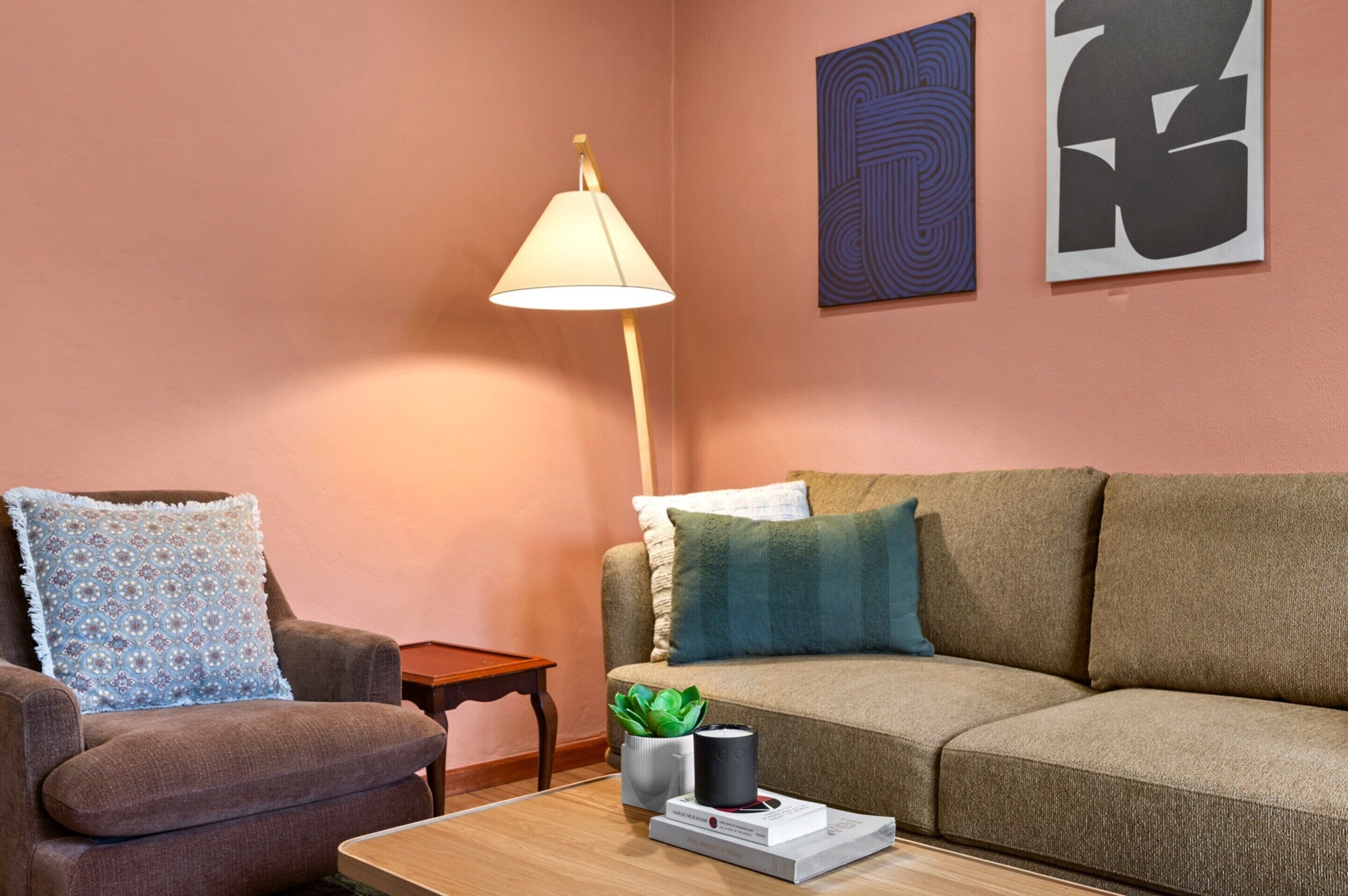 A living room with a brown sofa, a blue patterned armchair, a floor lamp, and abstract wall art.