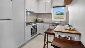 A modern kitchen with white cabinetry, a built-in oven, a gas stove, and a window providing a view of the outdoors. - Stylish 1 Bed Apartment in East Melbourne (Melbourne)