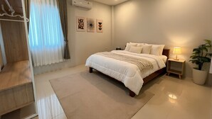 Une chambre à coucher comprenant un lit, des tables de chevet, une commode, un climatiseur fixé au mur, une fenêtre avec des rideaux et une plante en pot.