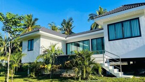 Uma casa moderna de dois andares com telhado plano, janelas amplas e um gramado bem cuidado com palmeiras.
