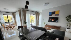 Uma sala de estar moderna com área de jantar, sofá, TV e janelas amplas.