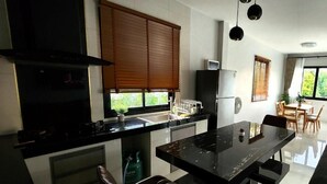 Cozinha moderna com ilha central, área de jantar com cadeiras e uma janela grande com persianas.