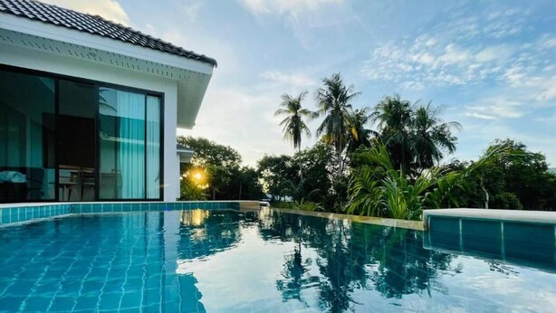 Piscina com azulejos azuis e límpidos, cercada por vegetação exuberante e um edifício moderno com amplas janelas.