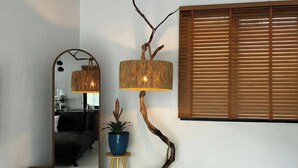 Un salon moderne avec un lampadaire au design incurvé, un miroir, une plante en pot et une fenêtre avec des stores.