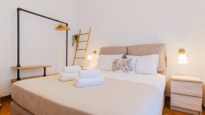 A neatly made bed with white linens, a bedside table with a lamp, and a wooden ladder against the wall.