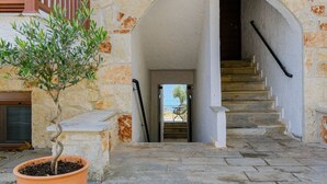 A stone building with a staircase leading to an upper level, a potted plant, and a view of the sea.