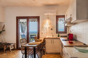 Une cuisine avec un coin repas, une vue sur la mer et un petit îlot central équipé d’un évier et d’une cuisinière.