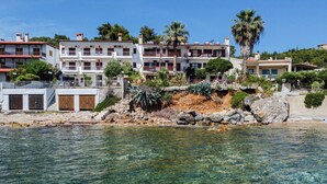 A coastal hotel with multiple floors, balconies, and a rocky shoreline.