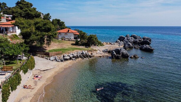 A coastal property with a beach, rocky shoreline, and a house with a red roof.