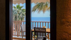 A balcony with a view of the sea, palm trees, and a chair.