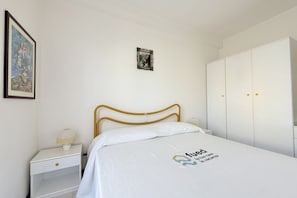 Et hotelværelse med seng, et natbord, en lampe, et klædeskab og et billede i ramme på væggen.