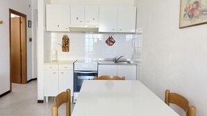 A kitchen with white cabinets, a stove, and a sink. There is a dining table with chairs.