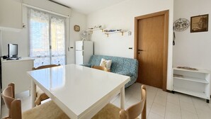 A compact living space with a dining table, chairs, a sofa, a refrigerator, a TV, and a door.