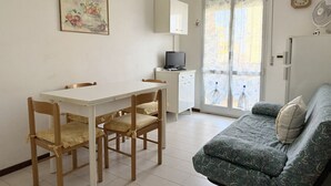 A room with a dining table, chairs, a sofa, a television, a cabinet, and a window with a view.