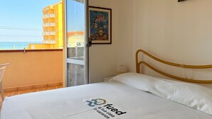 A hotel room with a bed, a window with a view of a building, and a painting on the wall.