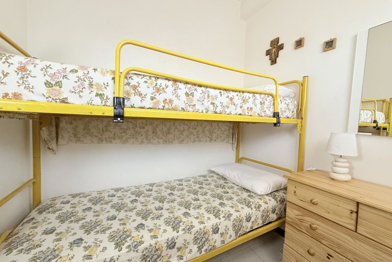 Un lit superposé avec une literie à motifs floraux, une commode en bois et un miroir.