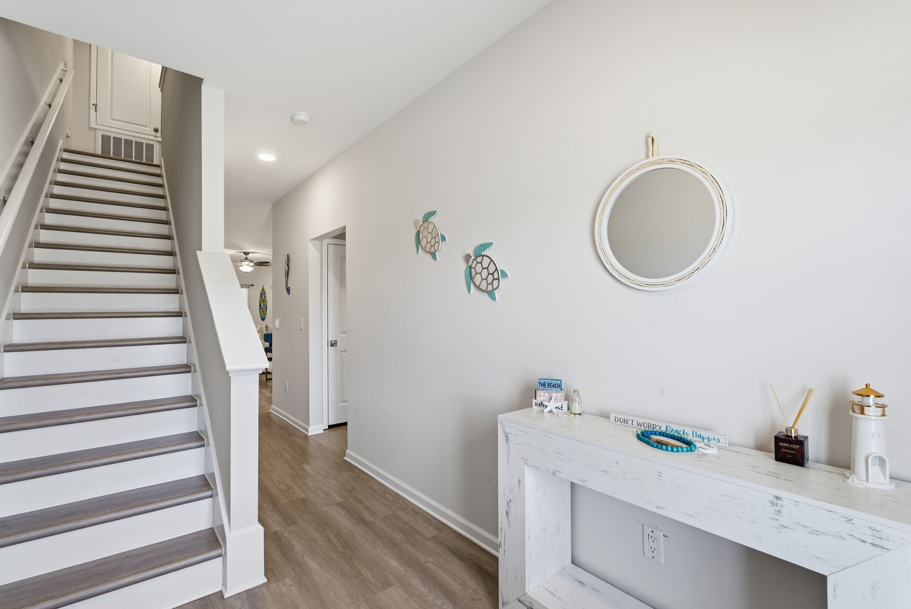 Un escalier menant à un couloir où se trouvent une console blanche, un miroir rond et des œuvres d’art décoratives accrochées au mur.