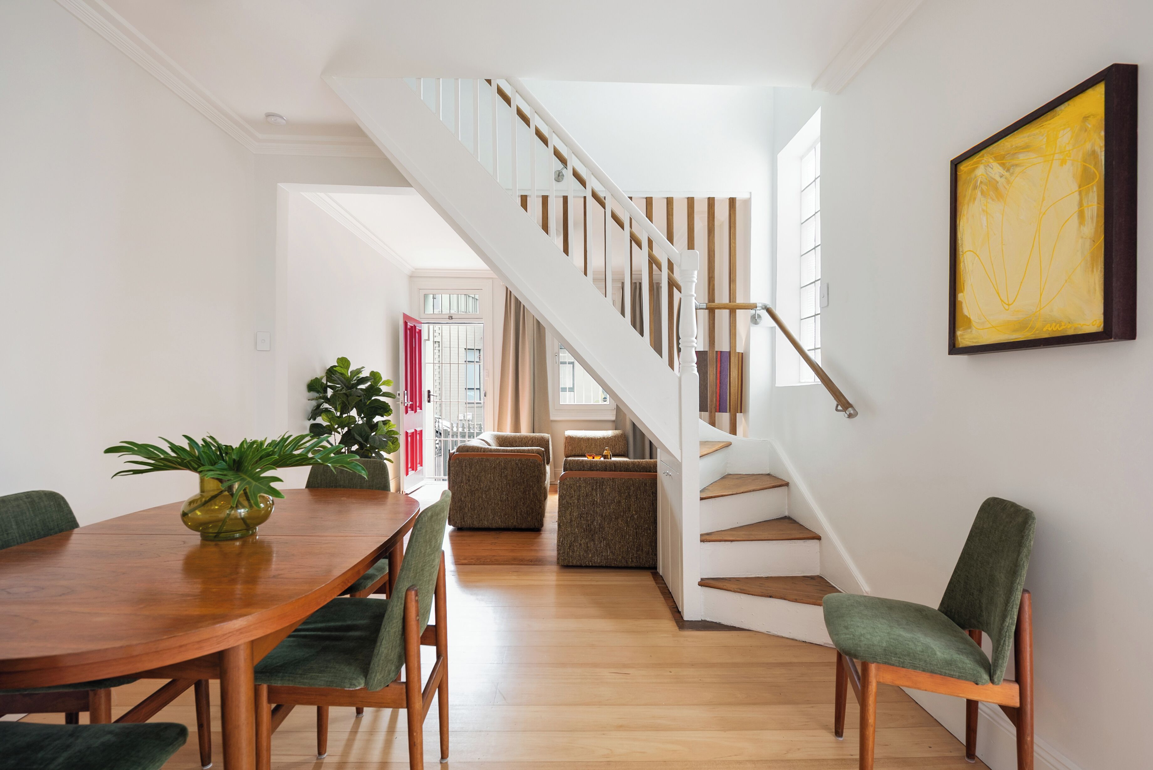 A dining area with a wooden table, green upholstered chairs, and a staircase with wooden steps and a white railing.